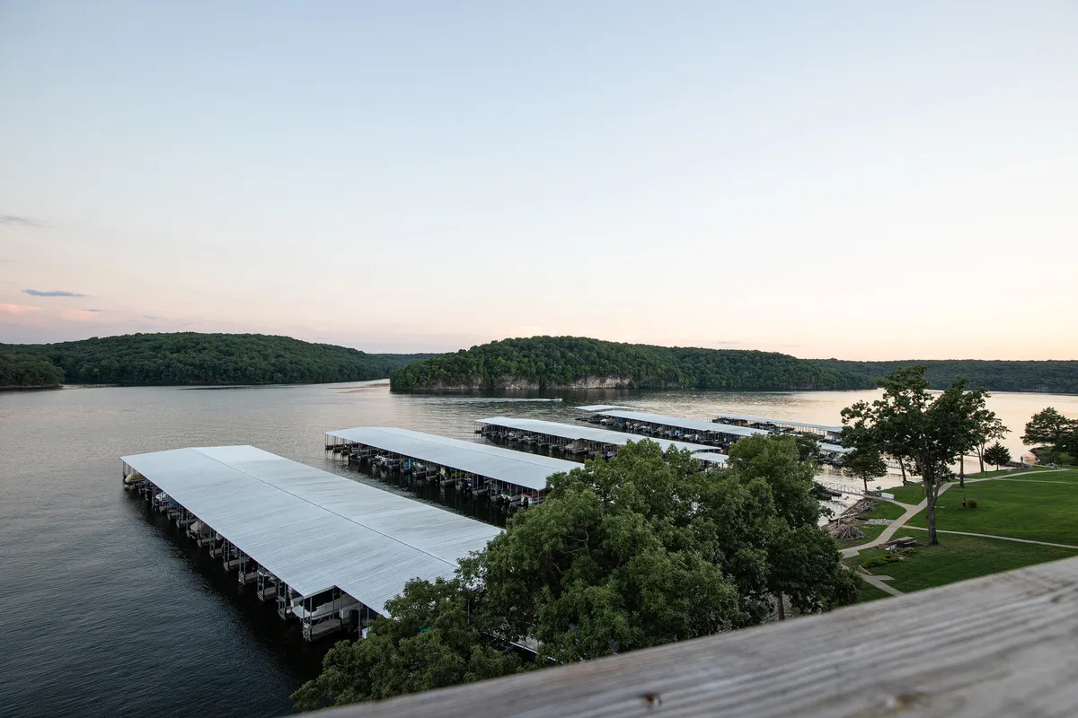 A wide-angle view of marina docks stretching into calm water, framed by lush greenery and distant rolling hills. The peaceful atmosphere sets the scene for boating, fishing, and waterfront relaxation.