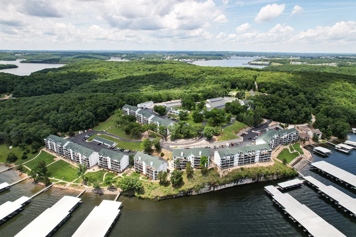 A tranquil lakeside scene featuring a marina with several docks, calm water, surrounding greenery, and nearby buildings. The serene setting invites boating, fishing, and relaxing by the water.