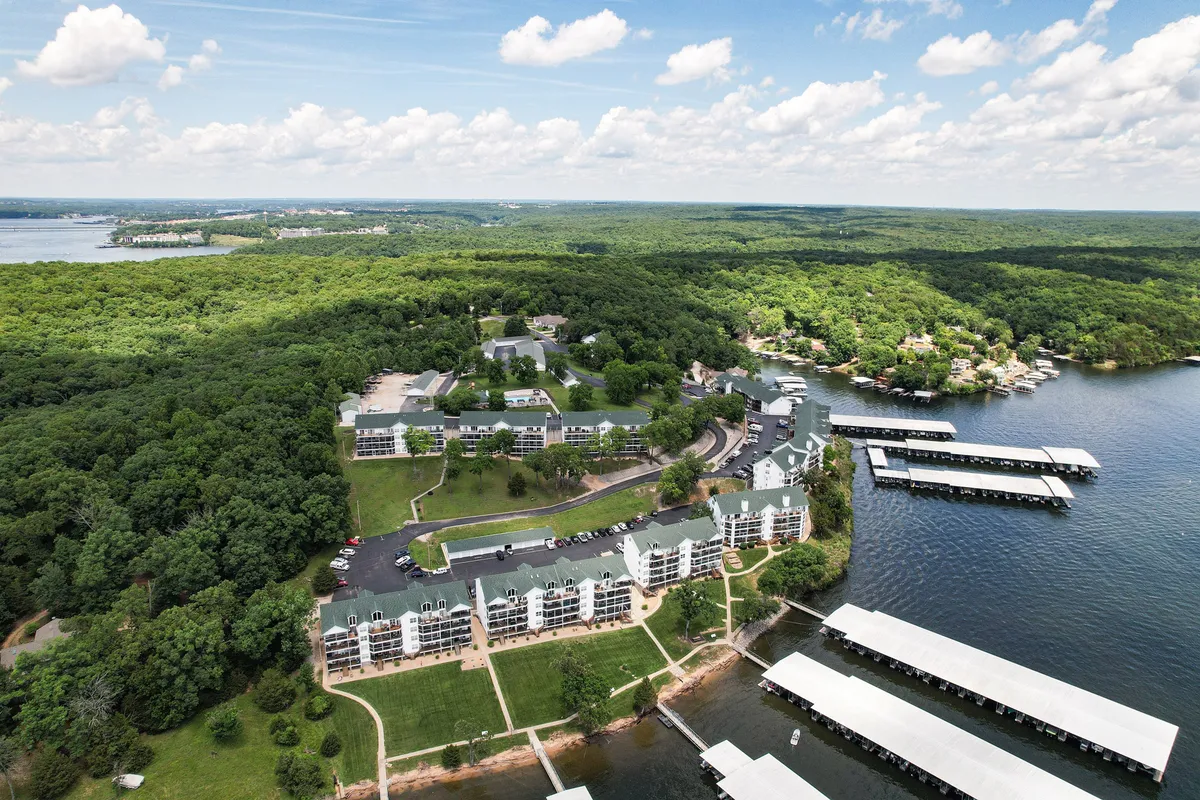 A scenic exterior shot of the lake, marina, surrounding greenery, and nearby buildings. Boats are docked along the marina, and the lush environment evokes a sense of adventure and outdoor exploration.