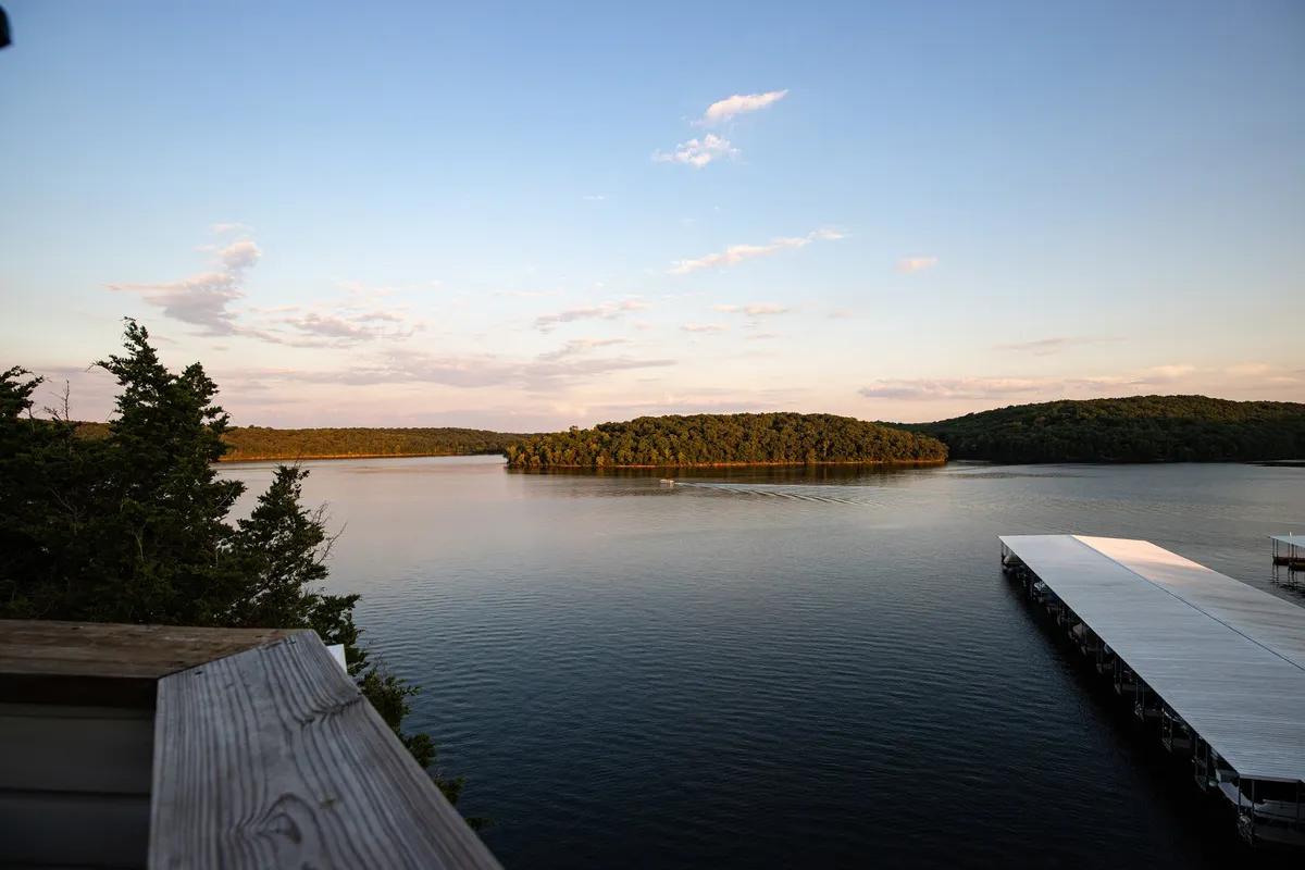 A peaceful view of calm water with an island in the distance and a pier stretching into the lake. The scene is set during sunset, with golden light reflecting off the water, inviting guests to imagine sunset boat rides and lakeside picnics.
