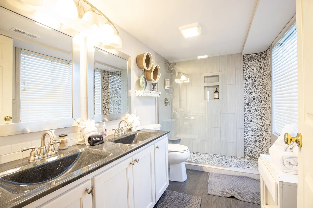 A bright, modern bathroom featuring dual sinks, large mirrors, a glass shower enclosure, and textured wall tiles. The space is both functional and stylish, reinforcing a sense of thoughtful, modern design.